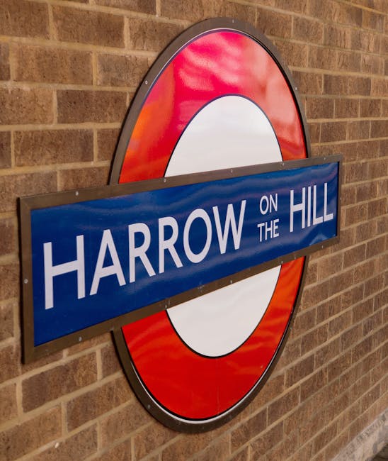 A round London Underground style sign mounted on a brick wall displaying the name 'Harrow on the Hill' in white capital letters on a blue rectangular background. The sign features a red circular border with a white central circle, characteristic of London Underground station signage. The brick wall behind the sign has a warm, reddish-brown tone with a textured and slightly uneven surface. The lighting appears to be natural, casting soft shadows and a slight sheen on the sign's surface. This urban setting suggests a location near a train or tube station, where passengers and commuters may encounter signage related to the area. The context of rubbish collection services, like those provided by Rubbish Collection Harrow, relates to efficient and independent waste disposal options near such transportation hubs, emphasizing the importance of alternative disposal methods within busy town or city environments.